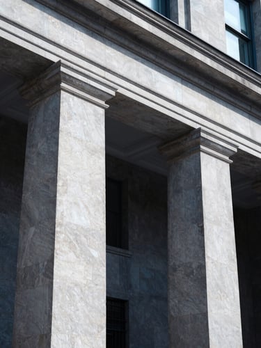 Low angle architectural view of a classic bank building facade with stone pillars, cool-toned daylight, sharp focus, deep navy shadows.