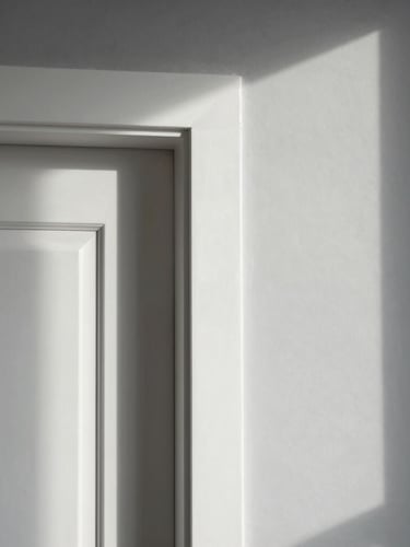 Straight-on architectural shot of a freshly painted white door frame meeting clean grey drywall, natural morning light casting soft shadows, crisp clean lines.