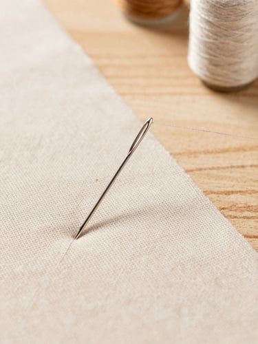 Macro detail of a silver sewing needle threading fine beige linen fabric on a clean, sunlit wooden workspace, high-end atelier style, 50mm.