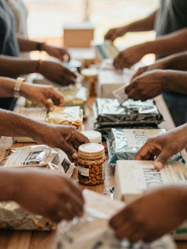 Candid mid-shot of diverse hands sorting donated items at a community pantry, natural daylight, shallow depth of field, warm documentary photography.