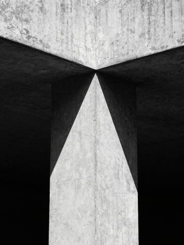 Extreme close-up of a high-contrast brutalist concrete structure with sharp geometric shadows, hard directional sunlight, desaturated black and white, 35mm film grain.