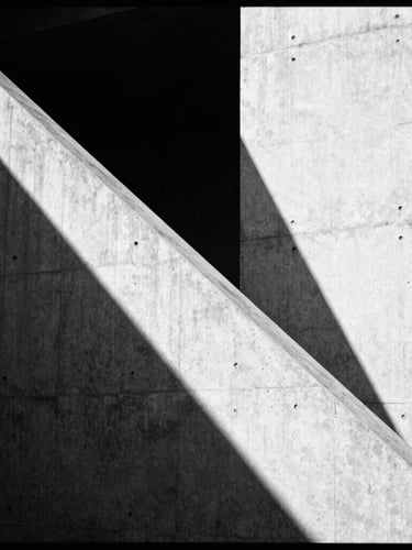 High-contrast editorial photography of a brutalist concrete structure, hard diagonal shadows cutting across the clean surface, desaturated black and white, 35mm film grain