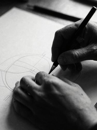 Raw close-up of hands working on physical design prototypes, harsh directional light, deep shadows, desaturated black and white