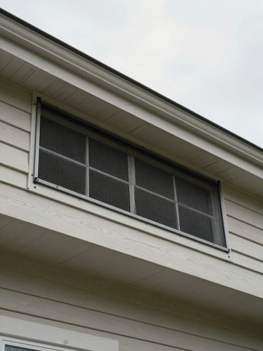 Wide shot of a sealed soffit vent on a suburban home exterior, overcast morning light, close framing on the heavy-gauge mesh fastened flush to painted wood trim, no people in frame