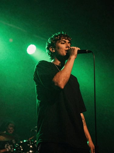 Low-angle gritty concert photography of an independent artist performing on stage under high-contrast neon green backlights, 35mm flash photography style.