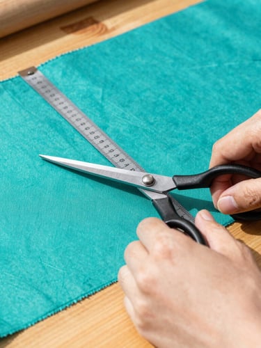 Close-up of artisan hands carefully measuring and cutting vibrant teal fabric with scissors on a wooden workshop table, warm morning sun filtering in