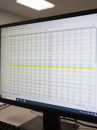 Close-up overhead view of a monitor displaying a data audit trail log with timestamps and classification flags, cool fluorescent office light, keyboard partially visible at bottom edge, clinical and precise