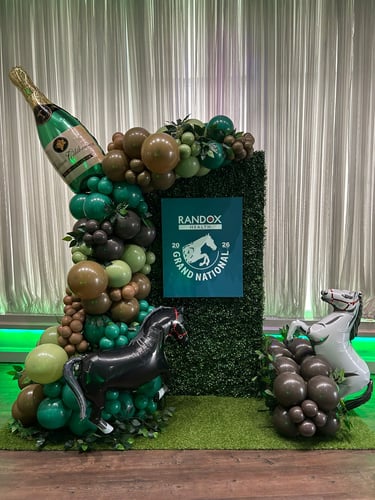 An elaborate Grand National event display features a large champagne bottle balloon, horse balloons, and a "RandoX Grand