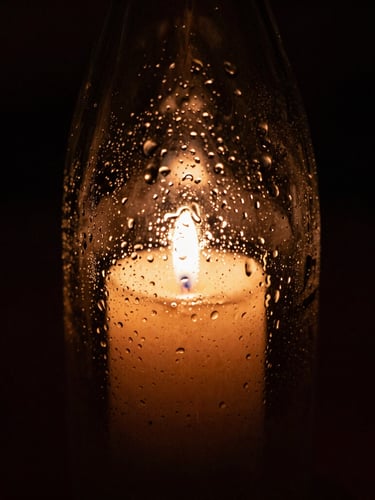 Tight macro shot of condensation on a dark glass bottle of biodynamic wine, warm candle-light reflecting on wet glass, deep shadows, 35mm film grain