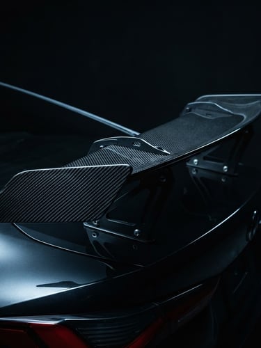Sleek automotive photography of a high-performance carbon fiber spoiler with dramatic studio rim lighting, cool dark tones, sharp detail.