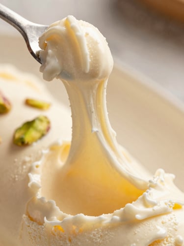 Macro close-up of thick, stretching Maraş ice cream being pulled with a metal hook, warm afternoon side-light, rich cream background, shallow depth of field
