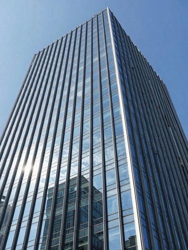 Low-angle architectural photography of a towering commercial glass facade reflecting a bright blue sky, sharp daylight, steel blue tones, crisp details.