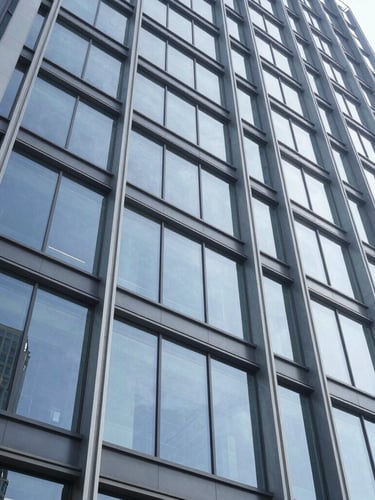 Low-angle shot looking up at a massive commercial building facade, crisp daylight reflecting off structural glazing, steel columns framing the glass, professional architectural photography