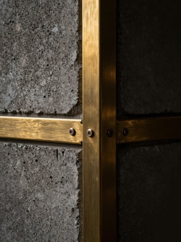 Dramatic close-up of textured concrete and brushed brass structural joints, high-contrast chiaroscuro lighting, dark luxury aesthetic.