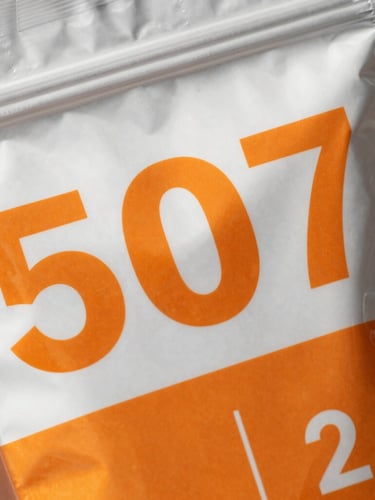 Macro detail shot of a custom-printed mylar bag showing sharp text and vibrant orange graphics, bright clean daylight on metallic foil textures, neutral background, high detail, 50mm