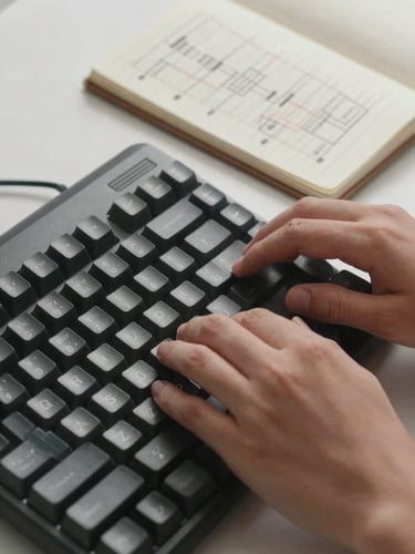 Close-up of hands typing on a mechanical keyboard next to a notebook with structured system flowcharts, crisp neutral studio lighting.