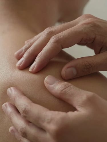 Tight macro close-up of hands demonstrating myofascial release on a shoulder, showing anatomical precision and absolute control under warm, soft lighting.