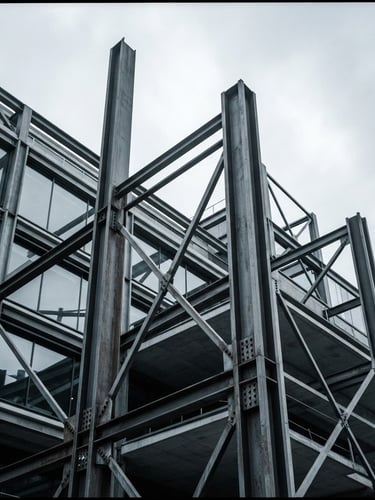 Sharp architectural photography of exposed structural steel columns against a cool overcast London sky, high contrast desaturated tones, 35mm lens