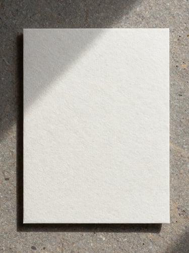 A top-down flat-lay of heavy embossed cotton paper stationery on a raw stone slab, soft diffused natural light, long gentle shadows.