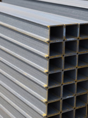 Close-up portrait shot of neatly stacked structural steel beams in a warehouse, sharp crisp daylight, cool steel tones, with a slight tilt.