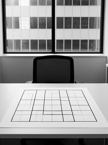 Crisp architectural photography of a structured office environment, focusing on a clean desk with a printed geometric planning grid, natural lighting, high contrast, symmetrical framing, 35mm
