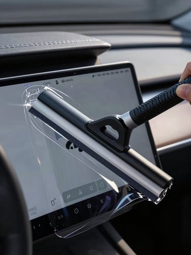 Extreme macro close-up of a squeegee applying clear protective film to a curved digital touchscreen inside a modern electric vehicle, sharp linear highlights tracing the dashboard contours, controlled low-key studio lighting.