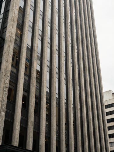 Wide environmental view of an investment-grade commercial building facade in São Paulo, shot from street level — structural concrete and glass textures filling the frame, natural overcast daylight, no people, no signage, austere geometric composition with strong vertical lines