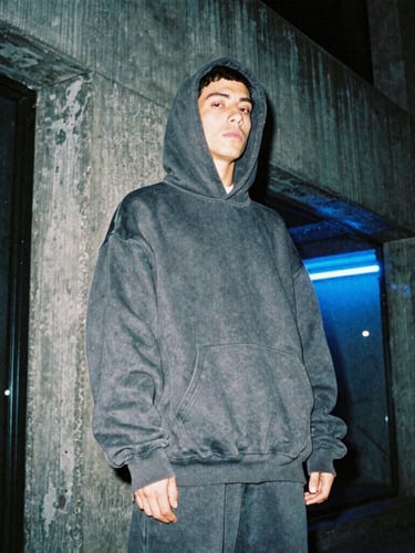 Moody low-angle shot of a hip-hop artist in an oversized heavy-weight dark grey hoodie standing in a brutalist concrete alley in Mexico City at night, midnight blue neon reflections, 35mm film.