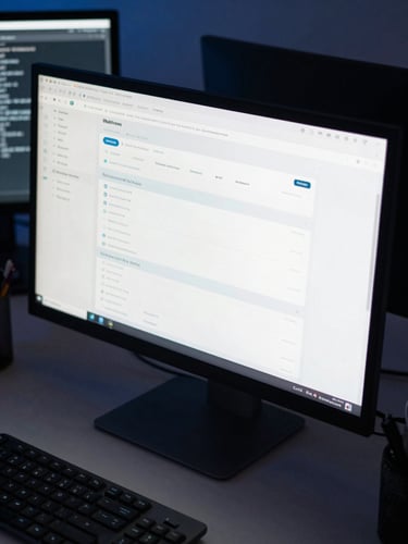 Close-up overhead view of a developer's desk, a monitor showing a Webflow CMS panel with structured content fields, a second screen with terminal output, cool blue-toned lighting, no people visible — the work itself front and center
