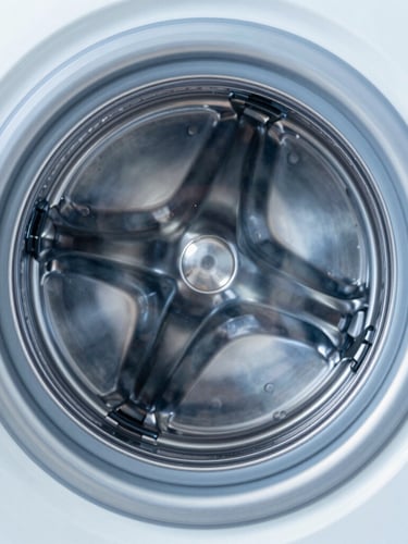 Symmetrical close-up of a gleaming stainless steel washing drum, bright high-key studio lighting with cool blue undertones, sharp macro focus