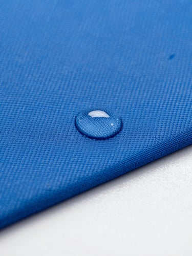 Macro shot of water droplets bead on high-performance blue technical fabric, bright cool-toned studio light, clinical focus