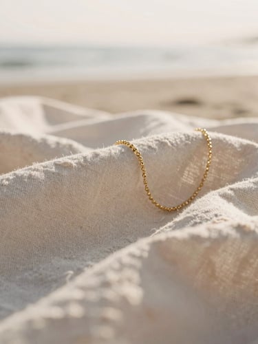 Tactile close-up of natural linen fabrics and delicate gold jewelry catching warm morning sunlight, soft focus background, coastal minimalist aesthetic