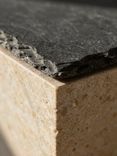 Extreme close-up of a flawless material junction where dark slate meets warm travertine stone, soft natural Mediterranean sunlight casting clean shadows.