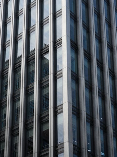 Abstract architectural detail of a modern corporate skyscraper facade with steel and dark glass panels, cool high-contrast lighting, sharp angles, minimalist composition.