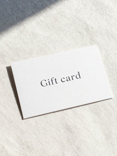 Minimalist high-end gift card on textured heavy paper, elegant typography, resting on a warm pearl-white linen surface, soft natural alpine daylight, glacier blue shadows, 35mm photography