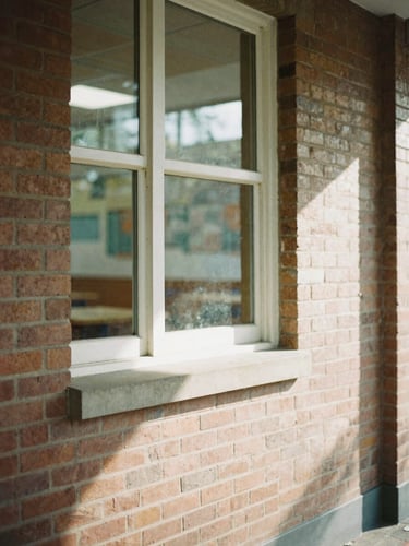 A quiet architectural detail of a community center window, soft natural daylight casting long shadows on warm brick, shallow depth of field, 35mm film aesthetic