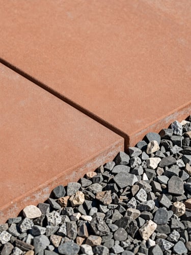 A crisp close-up of a modern terracotta-toned concrete paver joint meeting textured slate gravel, sun-drenched architectural detail