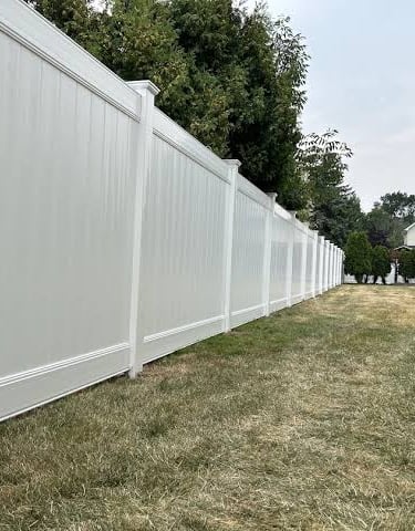 White vinyl privacy fence installed along a backyard lawn for residential security.