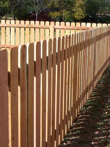 A classic natural cedar wood dog ear picket fence installed around a backyard lawn.