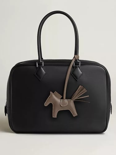 Hermes Elegant black leather handbag with a designer horse charm accessory and double top handles.