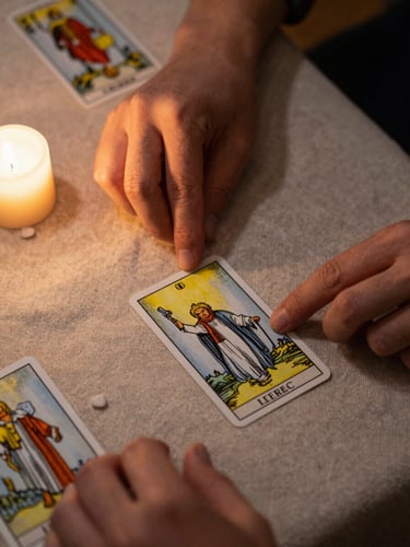 Close-up overhead framing, hands deliberately laying tarot cards face-up on a rough linen surface, candlelight from the left casting warm golden shadows across the cards, fingertips visible mid-placement, the rest of the table receding into soft darkness