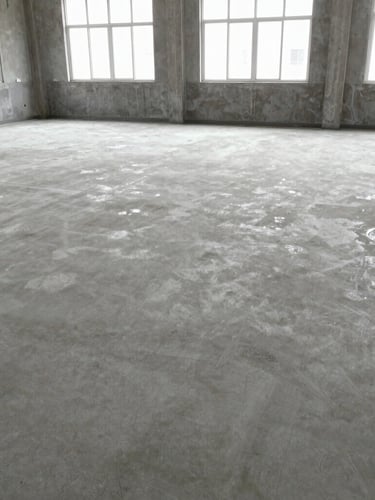 A clean, fully cleared commercial concrete floor after a soft strip demolition, bright natural light pouring through windows, orderly and ready for handover