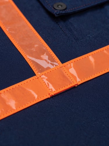 Macro shot of heavy-duty triple-stitching on deep navy workwear fabric with orange reflective safety tape, crisp workshop lighting, industrial product photography, 50mm lens