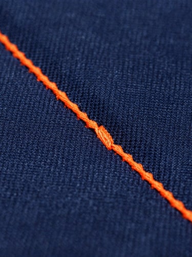 Macro shot of heavy-duty triple-stitching on a deep navy canvas fabric, safety orange thread, industrial quality, crisp focus
