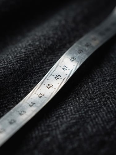 Extreme close-up on a silver measuring tape resting on dark charcoal wool fabric, dramatic studio lighting, sharp focus, 50mm lens