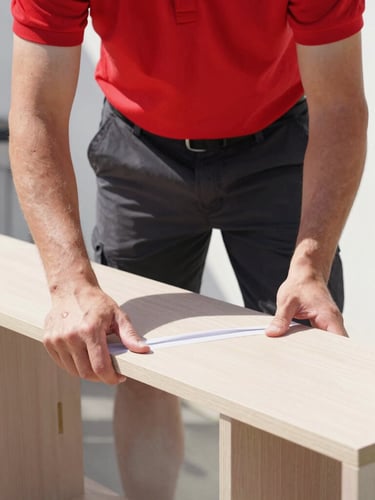 Portrait-oriented shot of a RapidMotion mover in red shirt and black shorts carefully wrapping a piece of furniture, bright natural daylight, high contrast, focused on hands and professional attire.