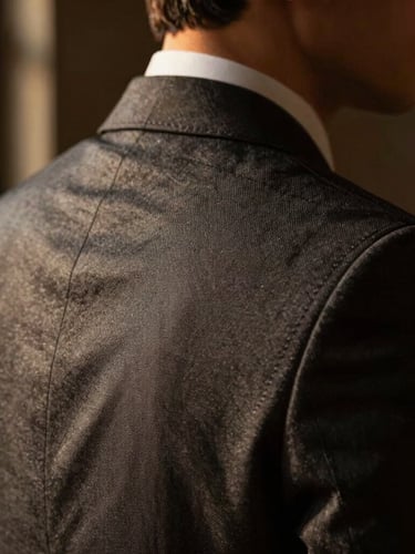 Medium close-up portrait of a tailored men's suit shoulder and collar, focusing on high-quality fabric texture and precise stitching, warm directional window lighting, moody dark background