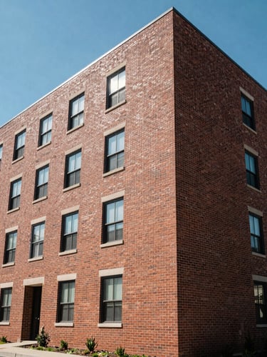 Wide-angle architectural shot of a clean, modern brick apartment building in Central PA under bright natural daylight, structured geometric lines, clear blue sky.