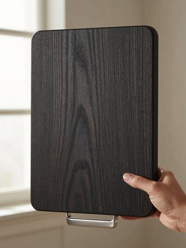 Hands holding a heavy, textured oiled oak cutting board with a brushed steel handle, soft directional window light