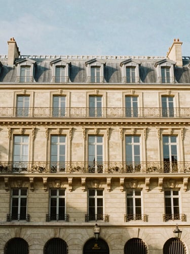 Wide architectural shot of a classic Haussmannian facade in Paris, sunlit warm afternoon light, soft shadows, 35mm lens editorial photography